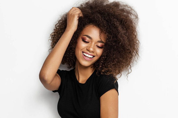 Beautiful smiling african american woman touching her afro hairstyle isolated on white background - Fotografie, Obrázek