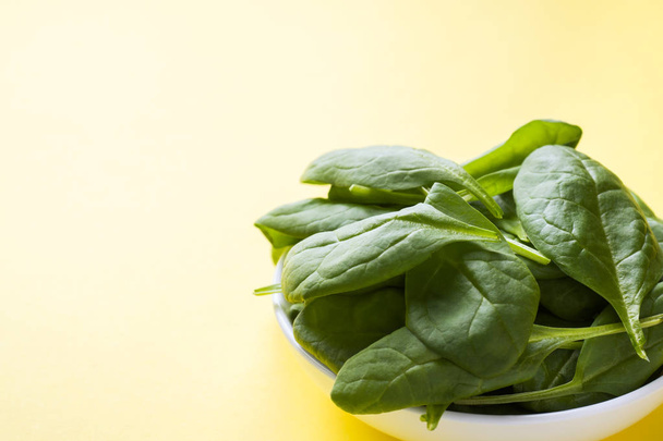 Fresh spinach leaves in a plate on a yellow background - Foto, afbeelding