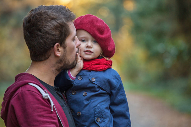 Father hugs and kisses daughter in the autumn park. They laugh and walk. - Foto, afbeelding