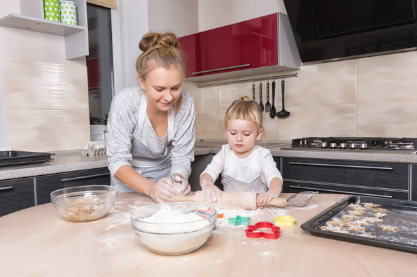 Happy family! A tiny daughter spends time with her mother in the kitchen to bake cookies. Mother's Day. - Foto, Bild