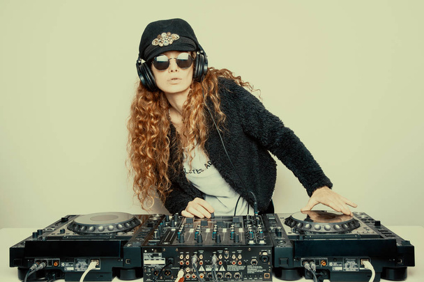 kifejező vöröshajú nő kalapot és napszemüveget DJ előtt fehér fal  - Fotó, kép