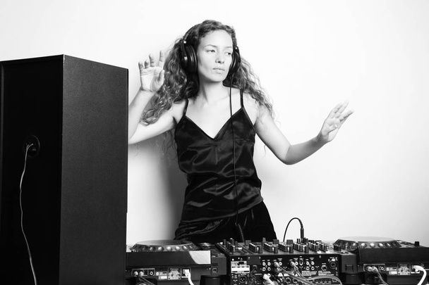 black and white shot of beautiful curly woman dancing while djing in front of white wall  - Photo, Image