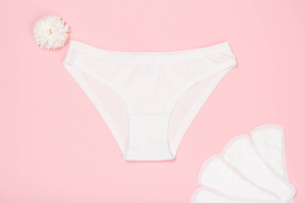 Hermosas bragas blancas con toallas sanitarias sobre fondo rosa. Ropa interior de mujer. Vista superior
. - Foto, imagen