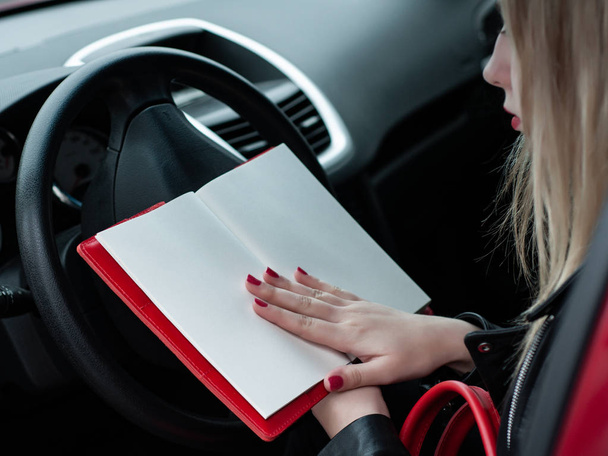 kaunis valkoihoinen tyttö punaisella muistikirjalla autossa
 - Valokuva, kuva