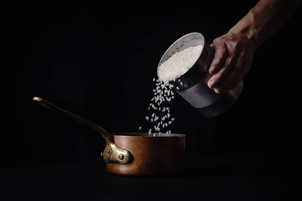 Female hand pouring arborio rice to copper saucepan for boiling  - 写真・画像