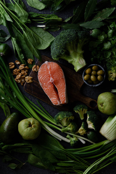 Fresh healthy vegetables with greens and fruits with walnuts and raw salmon steak on grey background  - Photo, Image