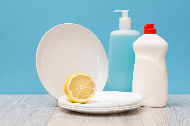 Bouteilles en plastique de liquide vaisselle, nettoyant pour vitres et carreaux, assiettes propres et citron sur fond bleu. Concept de lavage et de nettoyage
. - Photo, image