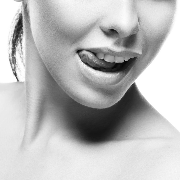 Monochromes Porträt eines jungen weiblichen Modells mit herausgestreckter Zunge auf weißem Hintergrund  - Foto, Bild