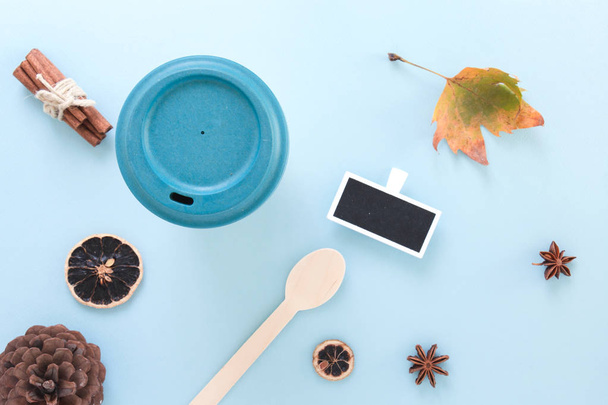 Bamboo reusable takeaway cup with lid on with autumn leaf, wooden spoon and other objects, flat lay on blue background. - Photo, image