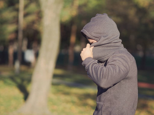 Mann versteckt Gesicht mit Kapuze an sonnigem Herbsttag im Park - Foto, Bild