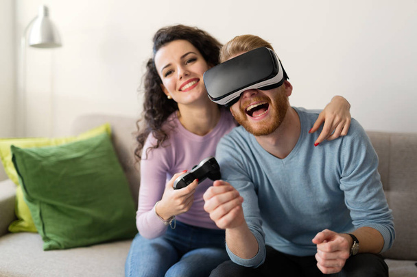 Happy young couple playing video games with virtual reality headsets at home - Fotó, kép