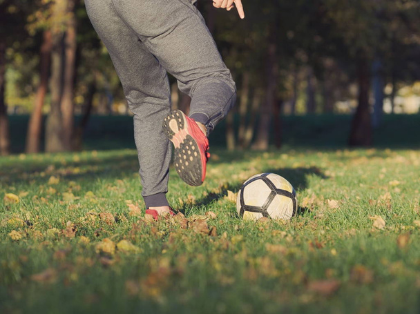Jalkapalloilija potkii jalkapalloa puistossa aurinkoisena syyspäivänä
 - Valokuva, kuva