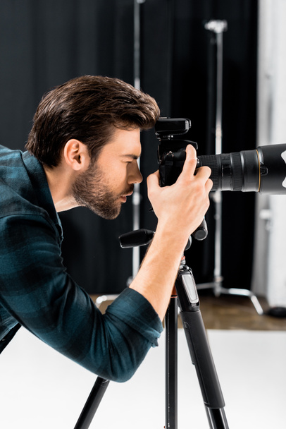 side view of handsome young photographer working with professional photo camera in studio  - Foto, Bild
