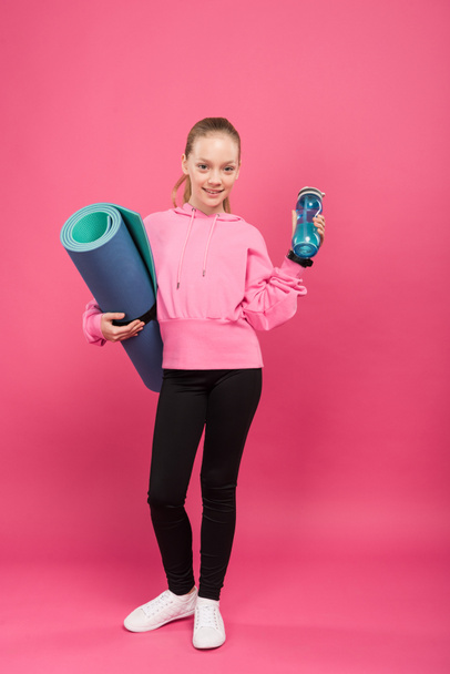 adorable child holding fitness mat and sports bottle with water, isolated on pink - Fotografie, Obrázek