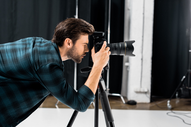 visão lateral do fotógrafo jovem profissional que trabalha com câmera no estúdio de fotos
 - Foto, Imagem