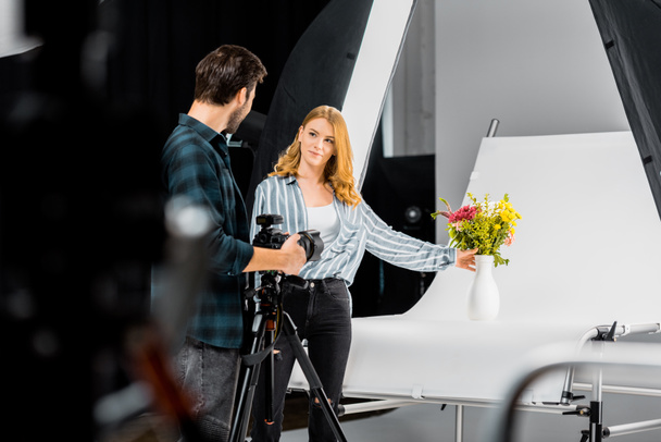 selective focus of young photographers looking at each other while shooting flowers in studio  - Zdjęcie, obraz