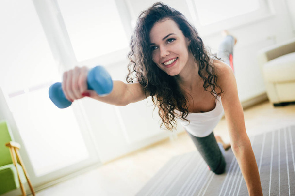Young attractive sportswoman doing fitness exercises at home - 写真・画像