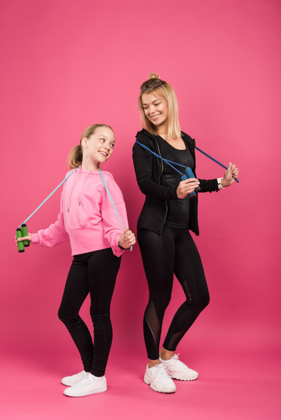 sportieve moeder en schattige dochter houden sprong touwen, geïsoleerd op roze  - Foto, afbeelding