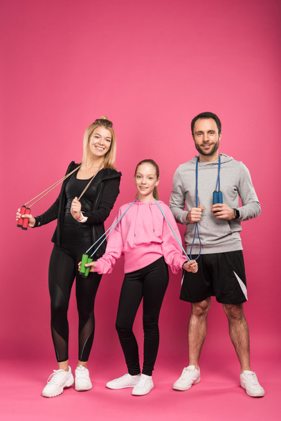 parents and daughter in sportswear holding skipping ropes, isolated on pink  - Fotografie, Obrázek