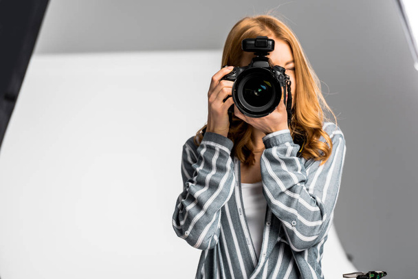 красивая молодая женщина-фотограф, снимающая профессиональным фотоаппаратом в студии
 - Фото, изображение