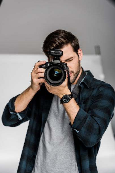 красивий молодий чоловічий фотограф використовує професійну камеру в фотостудії
 - Фото, зображення