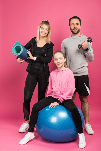 happy sportive family with fit ball, fitness mat and dumbbell isolated on pink - Fotografie, Obrázek