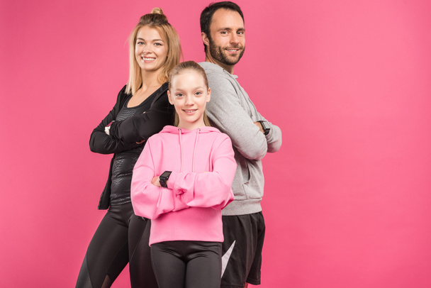 αθλητική οικογένεια ποζάρει σε αθλητικά ενδύματα με σταυρωμένα χέρια, απομονώνονται σε ροζ - Φωτογραφία, εικόνα