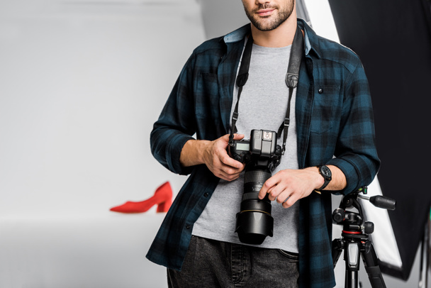 cropped shot of professional young photographer holding camera in photo studio  - Фото, зображення