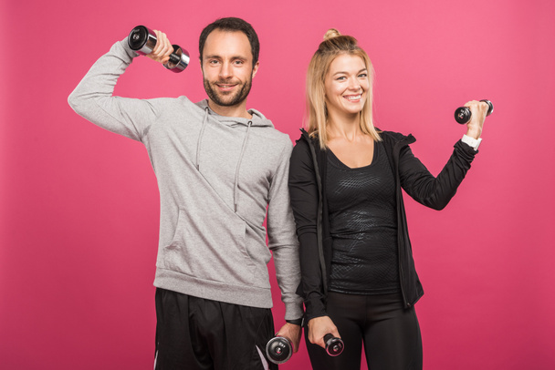 athletic couple training with dumbbells, isolated on pink - Foto, Imagen