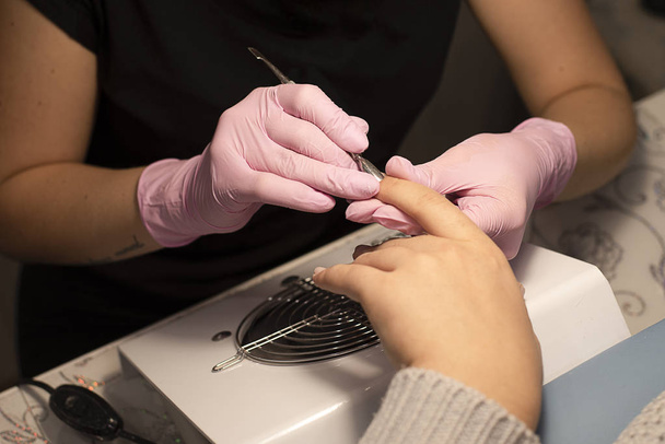 In the nail salon client manicurist in gloves handles nails with a spatula for manicure - Photo, Image