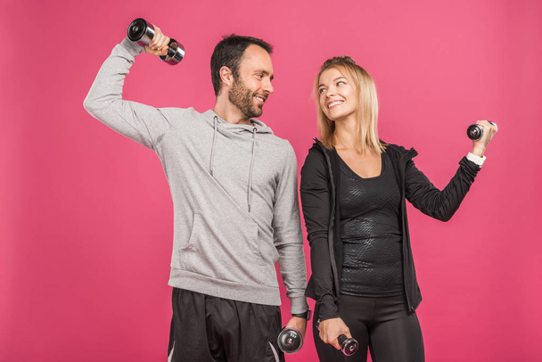 beautiful athletic couple training with dumbbells, isolated on pink - Foto, Imagem