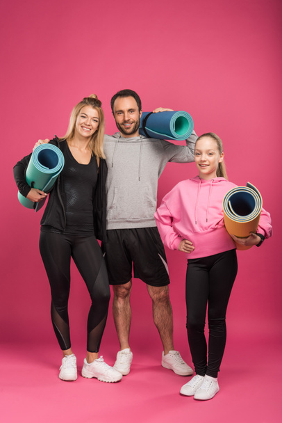 happy sportive family holding fitness mats, isolated on pink - 写真・画像