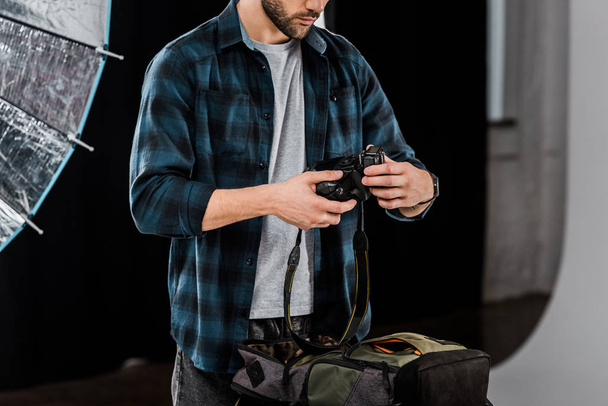 cropped shot of professional young photographer packing camera in backpack in photo studio  - Zdjęcie, obraz
