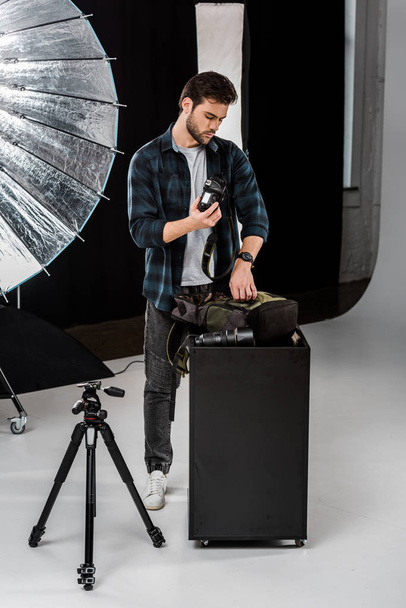 professional young photographer packing camera in backpack in photo studio  - Φωτογραφία, εικόνα