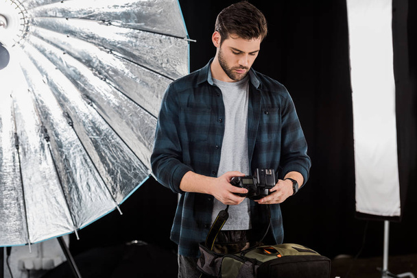 handsome young photographer packing camera in backpack in photo studio - Photo, Image