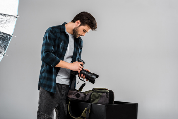 όμορφος νεαρός φωτογράφος κρατώντας φωτογραφική μηχανή επαγγελματική φωτογραφία σε studio - Φωτογραφία, εικόνα