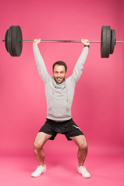strong sportsman training with barbell, isolated on pink  - Fotó, kép