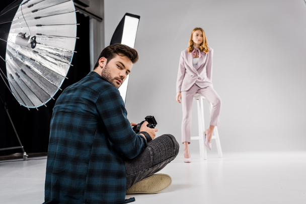 photographer sitting and looking at camera while beautiful female model posing in studio  - Zdjęcie, obraz