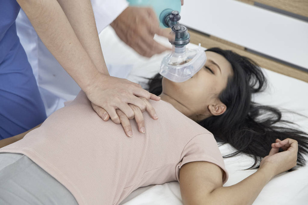 Manos de doctores dando masaje cardíaco y reanimación a una paciente femenina en el dormitorio, Concepto de Equipo Médico de Emergencia
 - Foto, imagen