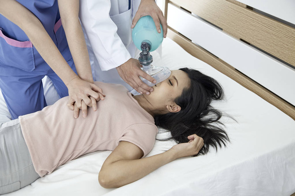 Manos de doctores dando masaje cardíaco y reanimación a una paciente femenina en el dormitorio, Concepto de Equipo Médico de Emergencia
 - Foto, imagen