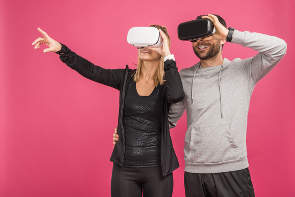 paar gebaren en het gebruik van virtuele realiteit hoofdtelefoons, geïsoleerd op roze - Foto, afbeelding