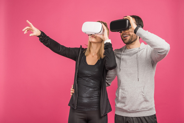 paar met behulp van virtuele realiteit hoofdtelefoons, geïsoleerd op roze - Foto, afbeelding