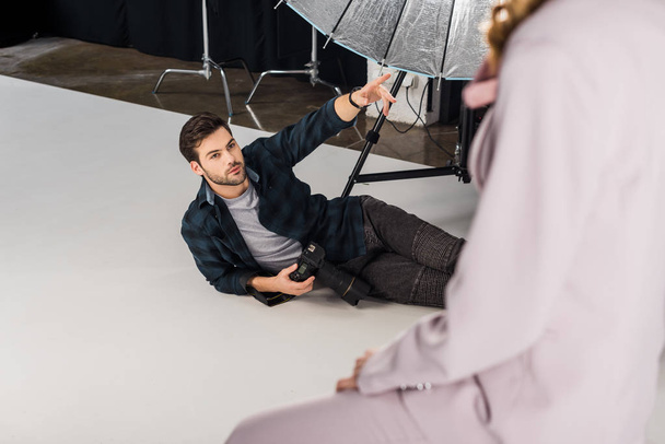 высокий угол обзора фотографа с камерой лежа и объясняя работу женской модели в студии
    - Фото, изображение