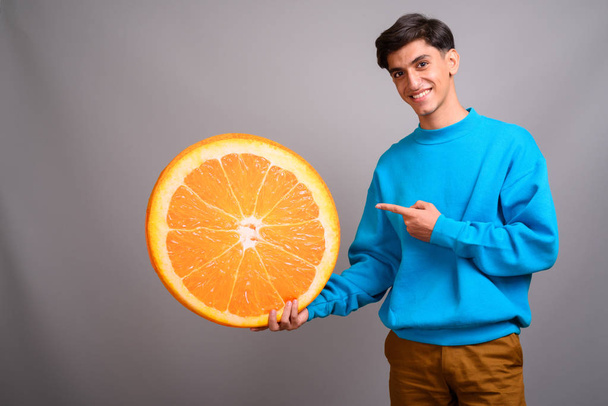 Młody Perski nastoletniego chłopca gospodarstwa duży kawałek owoc pomarańczowy - Zdjęcie, obraz