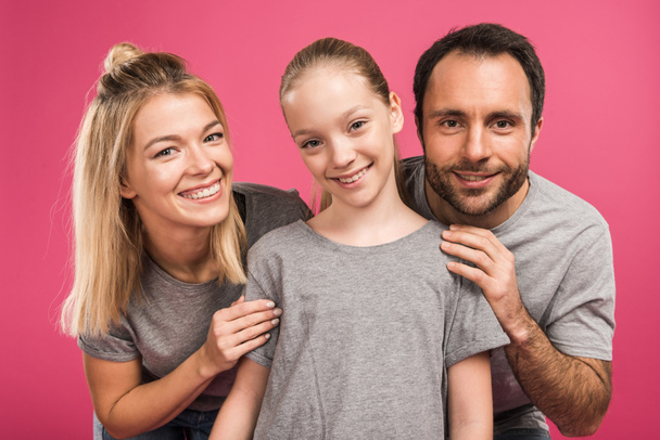 smiling parents hugging preteen daughter, isolated on pink - Фото, зображення