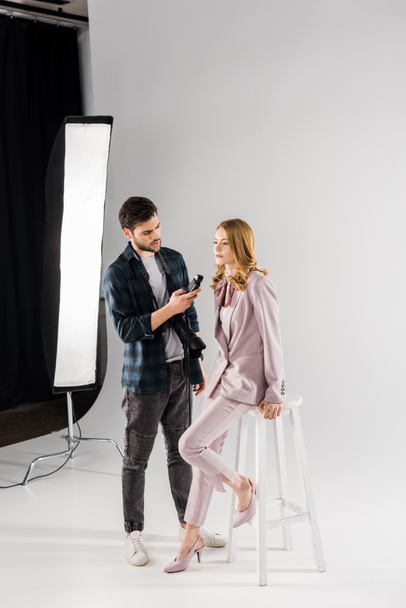 young photographer holding light meter and working with beautiful female model in studio - Foto, Imagem