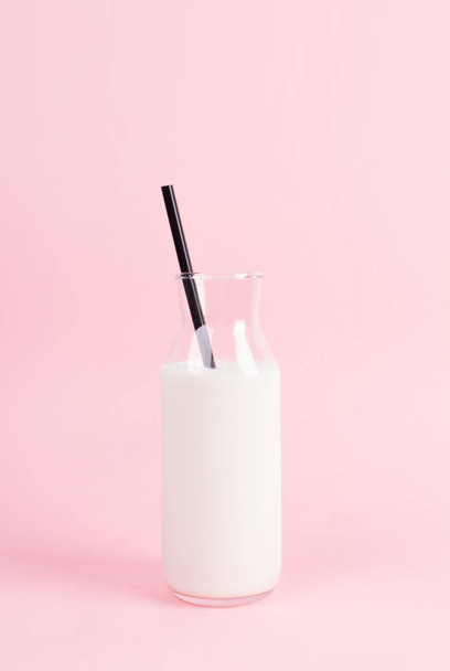 Fashionable bottle of milk on a pastel pink background. Black straw in the bottle. The concept of a minimalist breakfast. - Foto, Imagem