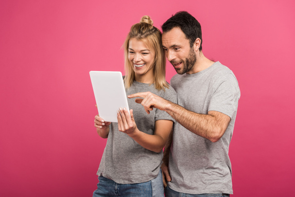 happy beautiful couple using digital tablet, isolated on pink - Fotó, kép