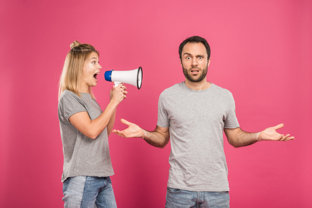 Wütende Frau schreit mit Megafon verwirrten Mann mit Achselzucken-Geste an, isoliert auf rosa - Foto, Bild