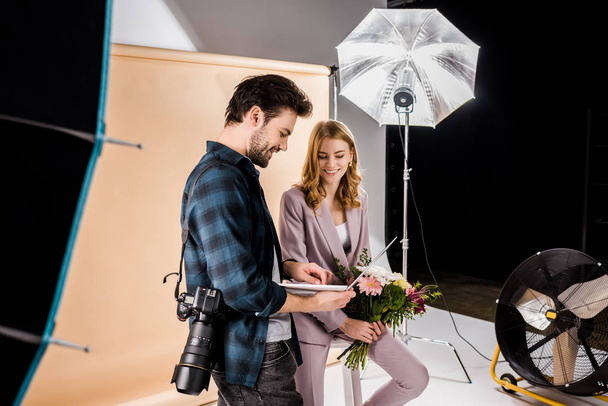 smiling young photographer showing laptop to beautiful female model in photo studio - Foto, imagen
